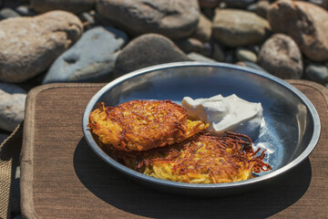 Potato pancakes cooked on a river trip. Dishes of Russian cuisine from vegetables with sour cream.