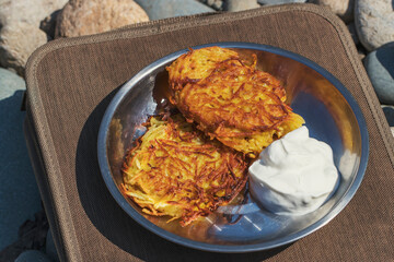 Potato pancakes cooked on a river trip. Dishes of Russian cuisine from vegetables with sour cream.