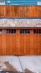 Vertical crop Brown wooden glass paned garage door against stone wall under balcony of home