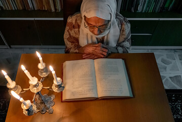 Fototapeta na wymiar Arabic muslim old woman reading books in her library at night with candles light