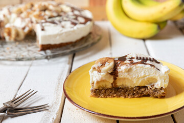 frisch gebackene Torte mit Bananen, Sahne, Schokosoße, Karamellsoße und Haselnussboden auf Tisch aus Holz in der Küche zum Kaffeetrinken