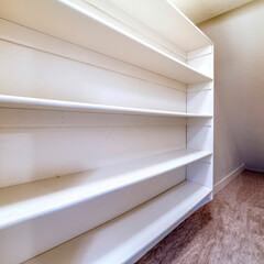 Square Small walk in closet with empty long cabinet shelves under slanted ceiling