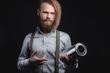 Portrait of a stylish bearded long-haired male salesman and dealer spare parts of the car in a shirt and suspenders. Holding a stainless steel exhaust muffler