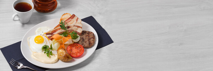 Breakfast of grilled sausages, crispy bacon with ciabatta, barbecue beans, fried eggs, fresh vegetables, grilled vegetables and cream cheese on a white plate and a light background. Banner. Copy space