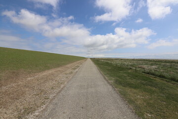 
Beautiful wide view over an elongated bicycle path along a dike. Photo was taken on a sunny May day with blue sky and white clouds.