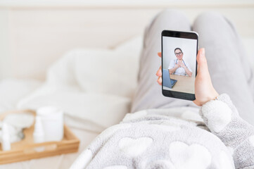 A woman is quarantined at home and is conducting a video conference with a virologist. The patient lies on the bed with a phone in her hands. Call from the doctor.