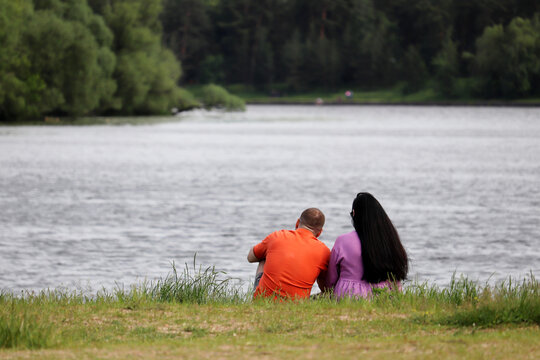 Love couple sitting on a lake coast in a park. Summer leisure, romantic date on a nature
