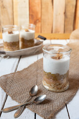 süßer gekochter zubereiteter Rhabarber im Glas unter Quark und Joghurt mit Walnüssen und Biscuit auf Tisch aus Holz in der Küche
