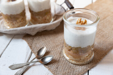 süßer gekochter zubereiteter Rhabarber im Glas unter Quark und Joghurt mit Walnüssen und Biscuit auf Tisch aus Holz in der Küche