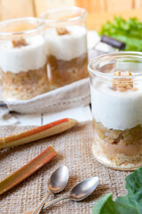 süßer gekochter zubereiteter Rhabarber im Glas unter Quark und Joghurt mit Walnüssen und Biscuit auf Tisch aus Holz in der Küche