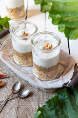 süßer gekochter zubereiteter Rhabarber im Glas unter Quark und Joghurt mit Walnüssen und Biscuit auf Tisch aus Holz in der Küche