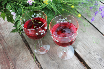 Midsummer night's dream strawberry elderflower cocktail, and wild blue and yellow flowers on the wooden board background. Two glasses of red wine with berries. Selective focus. Copy space
