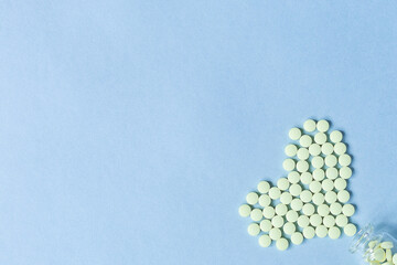 Yellow round tablets lie in the shape of a heart poured out of a glass bottle on a pastel blue background. Selective focus. Concept of health care, treatment and prevention of diseases. Space for text