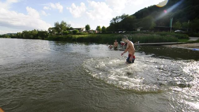Ein junger Mann l&auml;uft ins Wasser macht ein Salto im See 