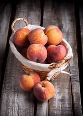 Peaches fresh vibrant color front view arrangement in knitted basket on dark rustic wooden kitchen table studio shot