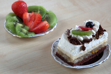 Cake with cream, pieces of chocolate and fruits at the top macro, pices of strawberries and kiwi fruits on decorative plate in soft focus