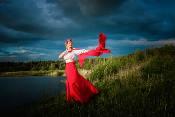 A slender caucasian girl in a red skirt and white blouse is dancing with a red shawl in her hands...