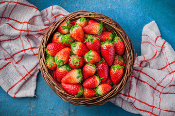 Strawberries fresh overhead colorful arrangement in woven basket on red and white kitchen cloth and rustic blue table studio shot