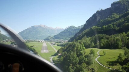 Aerial view of abandoned airport between mountains, small private plane landing on runway. Flying over rural, green scenery and rural suburb in Mollis, Switzerland.
