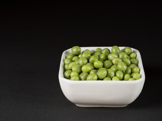 Organic green peas in a white bowl. Black background.