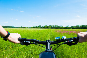 Fototapeta na wymiar Handlebar from a Bicycle with men's hands, on the background of a summer meadow, riding a mountain bike on a path, in the countryside.
