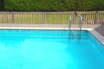 Modern swimming pool with pool cover for protection dirt rolled up and pool ladder in garden.