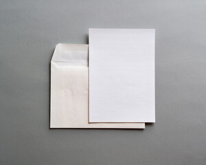 An empty, white, paper card for invitations or greetings and a white envelope on a gray , textured background.  Mock-up. Stylized stock photos. The view from the top.