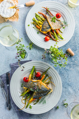 top view of delicious fish with vegetables on white plates and wine glasses on grey surface