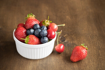 Fresh, delicious strawberries, blueberries and cherries in a white round bowl.