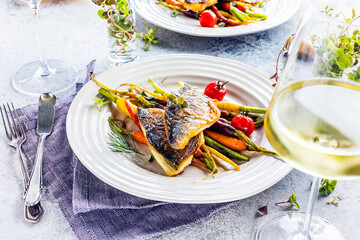 top view of delicious fish with vegetables on white plates and wine glasses on grey surface