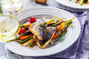 top view of delicious fish with vegetables on white plates and wine glasses on grey surface