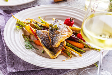 top view of delicious fish with vegetables on white plates and wine glasses on grey surface