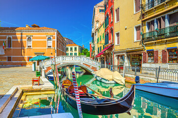 Fototapeta na wymiar Venice cityscape with gondola and motor boats moored on narrow water canal Rio dei Frari, colorful buildings and stone bridge, Veneto Region, Northern Italy, blue sky background in summer day