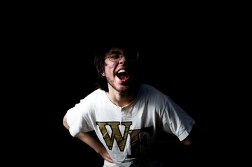 Fototapeta premium Young man being goofy towards the camera in a black backdrop