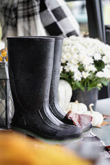 Black rubber rain boots, or wellies, sitting on front porch decorated for autumn.