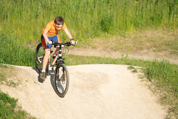 Naklejka premium Boy in sunglasses riding a bicycle from a hillock