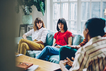 Serious women listening to black speaker sitting on couch