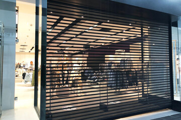 black shutted iron gates of shop in shopping mall due to restrictions of lockdown. Turned on light from closed doors. Preparation for opening after ending of lockdown.