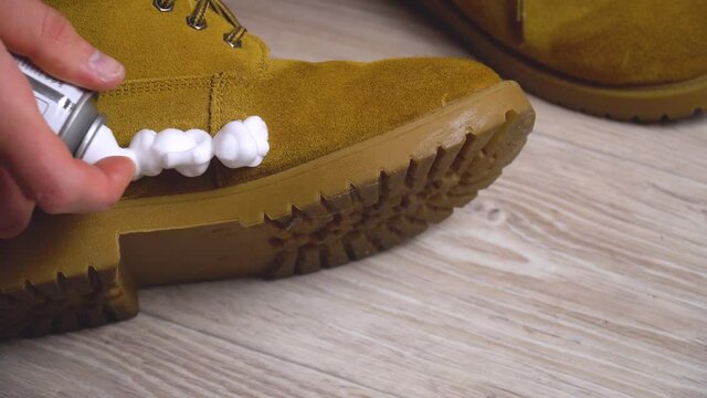 man's hand applies cleaning foam to dirty brown nubuck shoe and brushes it