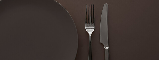 Empty plate and cutlery as mockup set on dark brown background, top tableware for chef table decor...