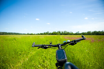 Fototapeta na wymiar Bicycle handlebar on the background of a summer meadow and path, mountain Biking on a dirt road, countryside.
