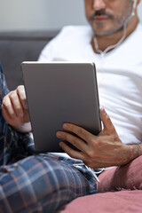 man holding using digital tablet and headphones in bed at home with pijama. Online education, working, video call