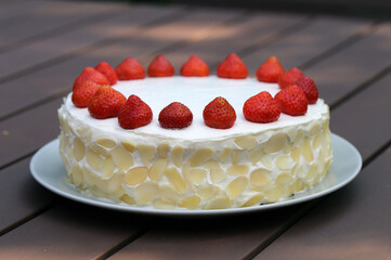 Fresh and delicious homemade summertime theme strawberry, almond and cream cake. Topped with whipped cream, fresh berries and almond slices. Cheerful closeup color portrait image of the cake.