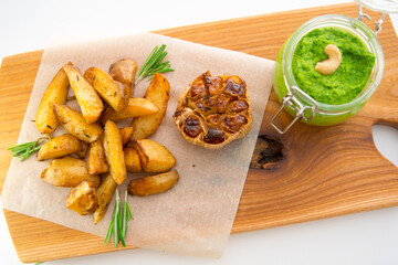 Baked potatoes with rosemary, garlic and pesto on a wooden board