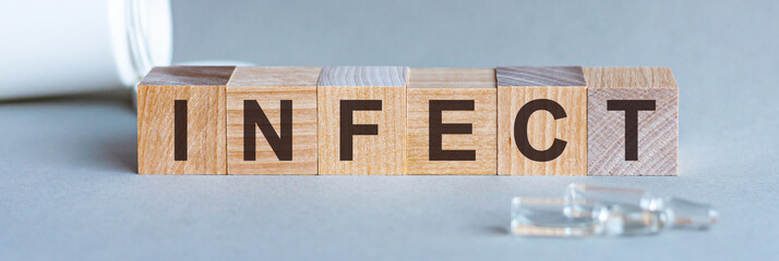 Word INFECT. Infect text on wooden blocks. In front of a row of cubes are ampoules, in the background - white plastic packaging from tablets, the cubes are located on a gray surface. Concept Image.