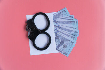 top view handcuffs with money in an envelope on a pink background