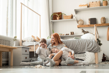 Young family resting together in parent's bed.After the pillow fight, a lot of feathers. Happy boys. Concept of maternal love, parenthood, happy family.