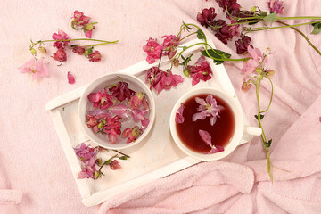 Flower composition. Cup of tea with pink flowers on a white wooden tray, aromatherapy and soothing effect, flat lay, lifestyle concepts, selective focus