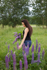 A girl with a bouquet of lupine is standing in a meadow. Lupine is blooming around.