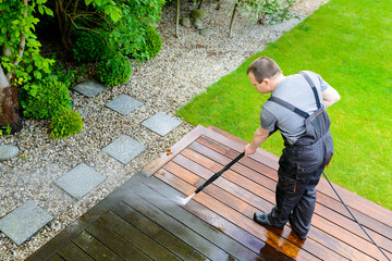 power washing - man cleaning terrace with a power washer - high water pressure cleaner on wooden...